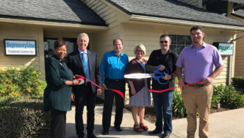 people standing in front of office holding red ribbing and giant scissors